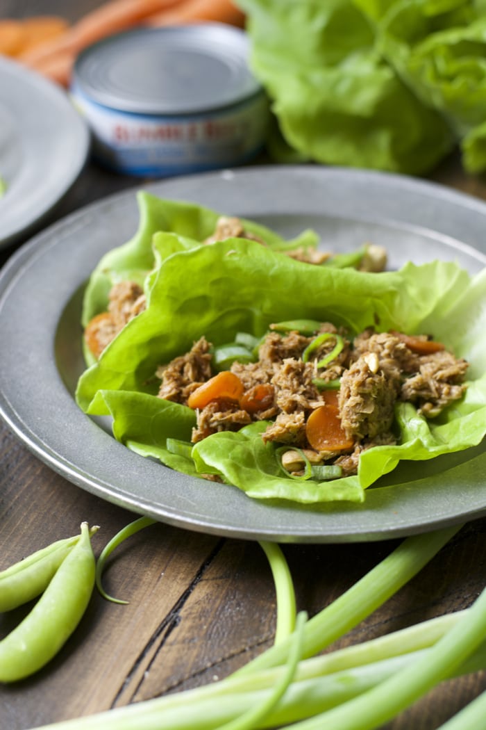 healthy lettuce wraps on a plate with a can of tuna and veggies in the background and foreground 