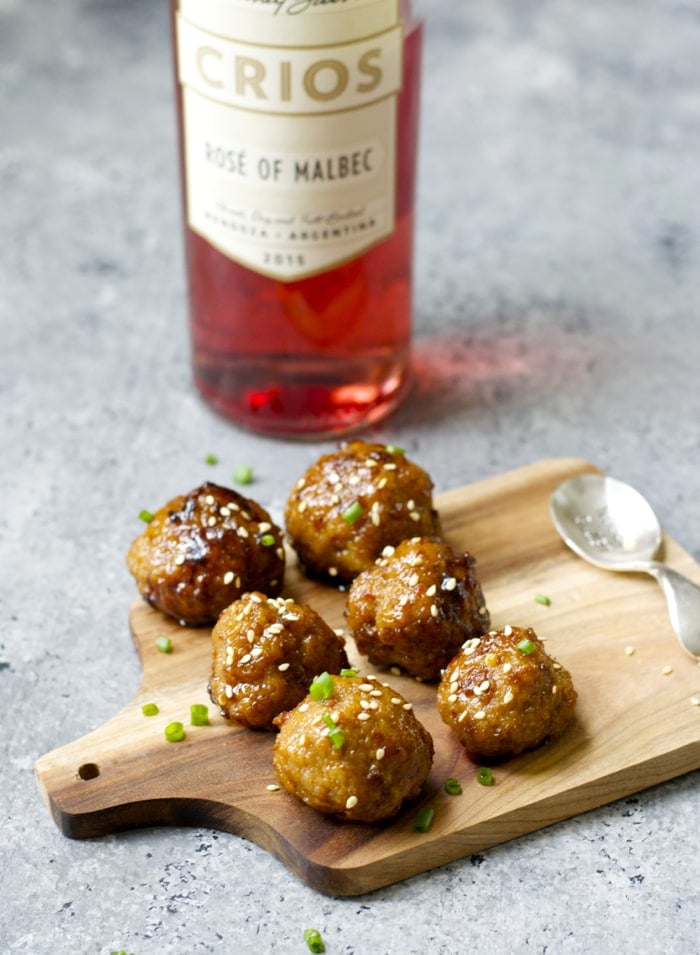 a cheese board with six Asian meatballs. a bottle of rose wine is in the background. 