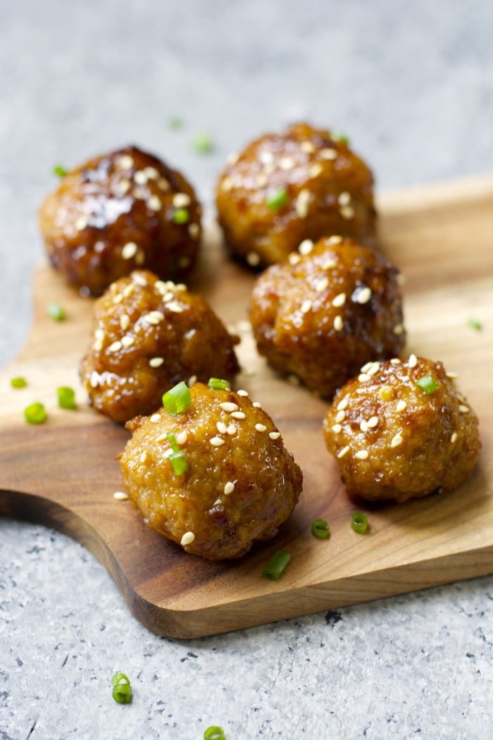 six asian style meatballs with spicy asian sauce on a wood cheese board 