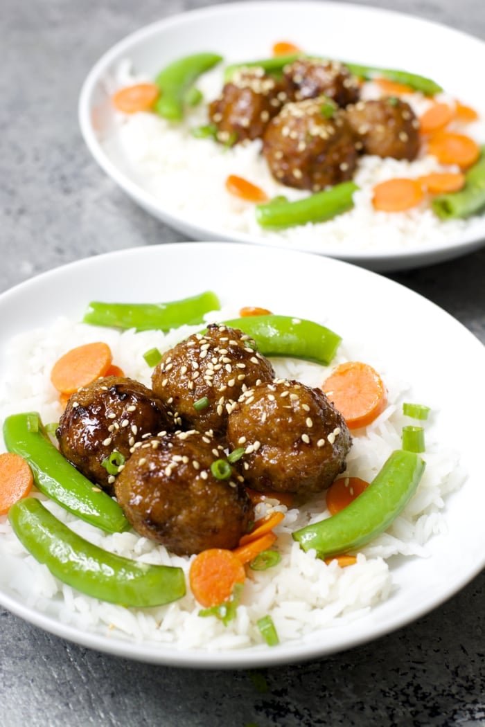 two plates of rice, veggies, and spicy asian style meatballs