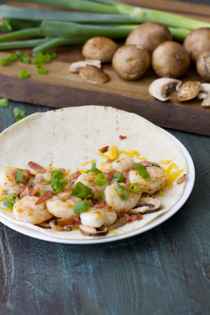 A bacon and shrimp quesadilla on a plate, open to show the fillings. 