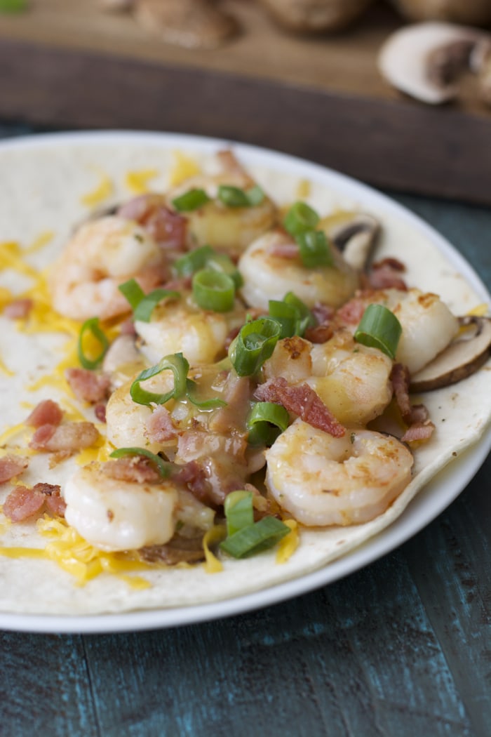 A bacon and shrimp quesadilla on a plate, open to show the fillings. 