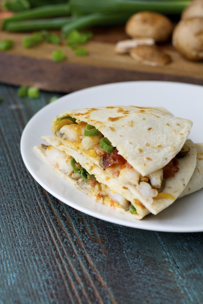 A homemade quesadilla that's been cut in half and stacked on itself on a white plate. 