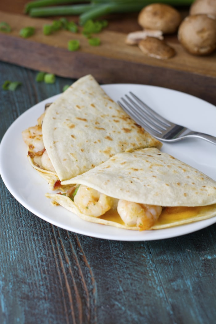 A shrimp and bacon quesadilla, cut in half on a white plate. 