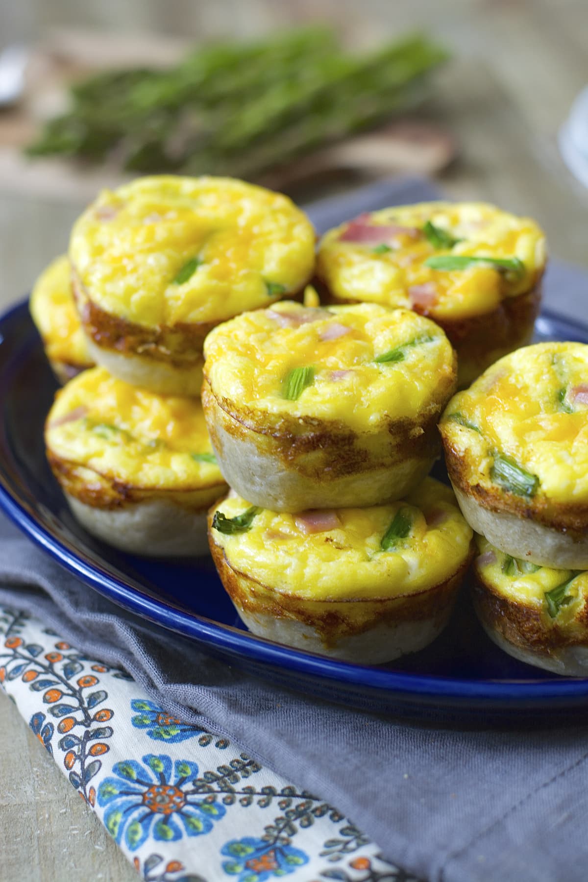 A pile of ham and asparagus mini breakfast quiche on a blue platter. 