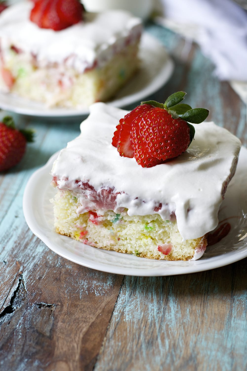 close up of a slice of strawberry funfetti cake on a white plate. Another cake slice is in the background. 