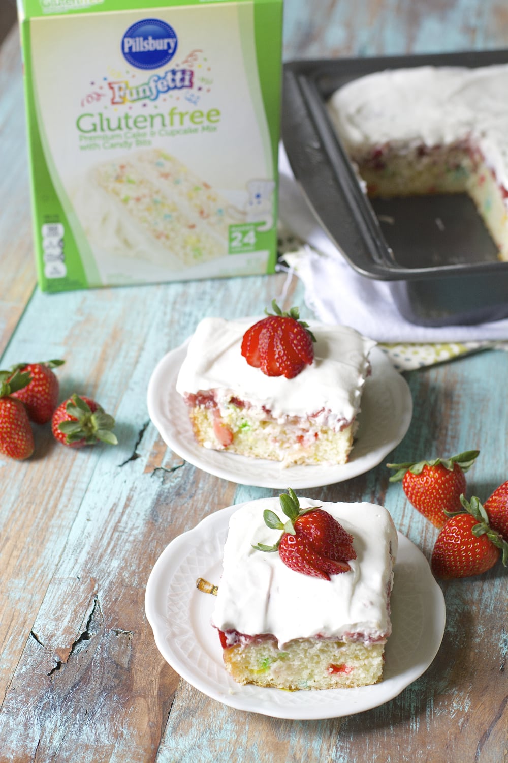 two slices of strawberry poke cake on white plates with box of cake mix in the background