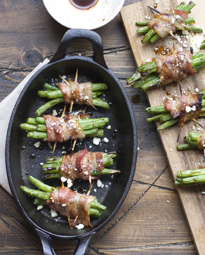 Overhead view of green beans wrapped in bacon in a cast iron skillet and on a cutting board 