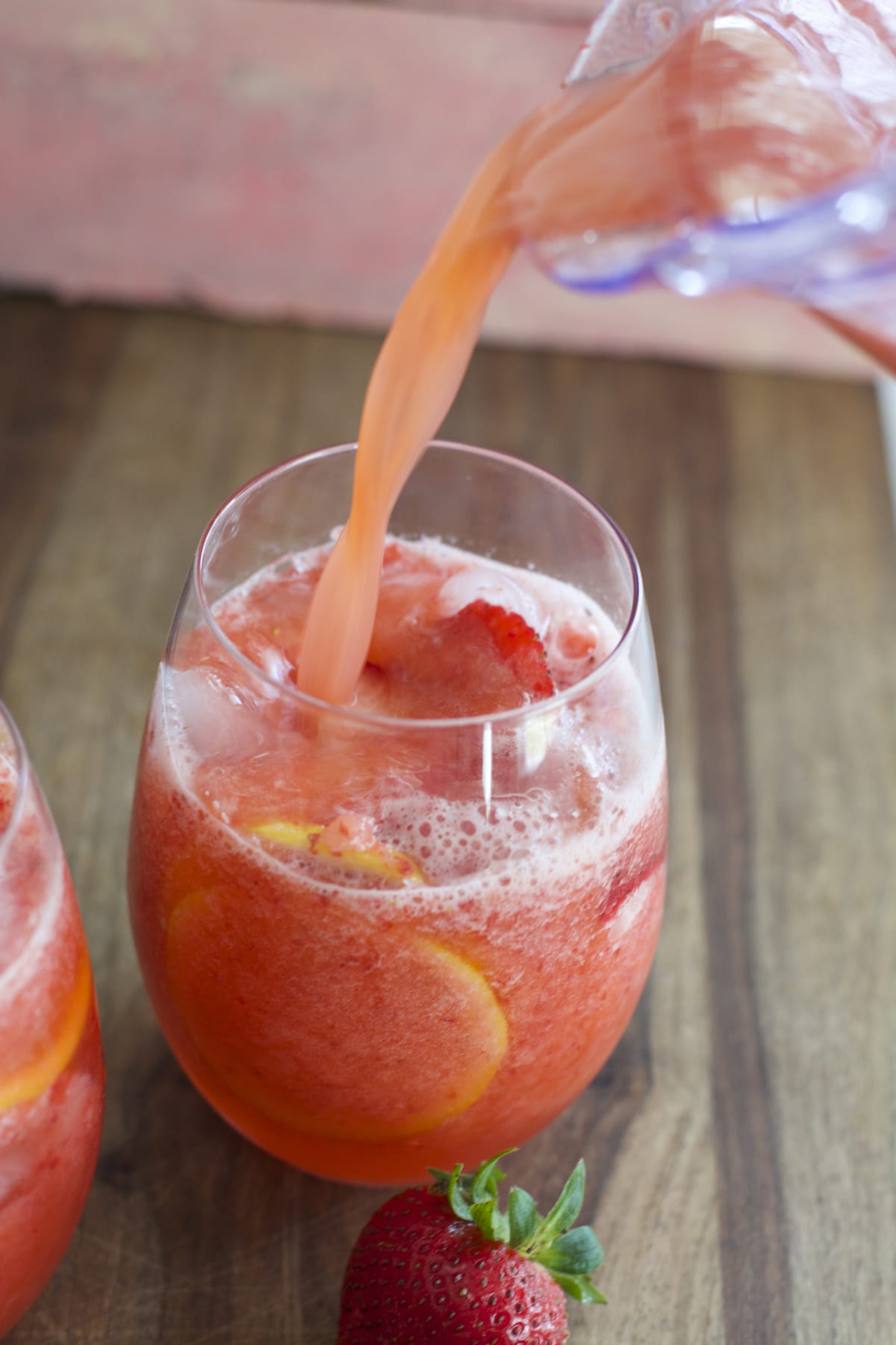 a pitcher of frozen lemonade with strawberries pouring into a glass with sliced lemons and berries