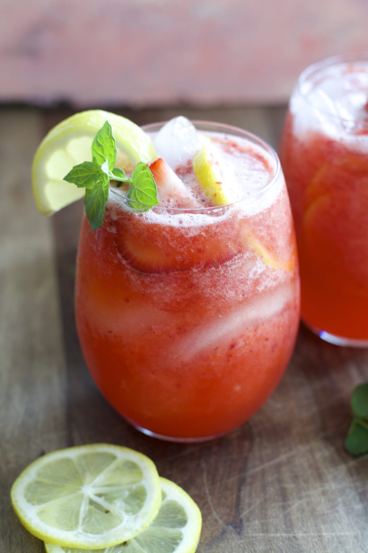 glass of strawberry lemonade garnished with mint leaves and lemon wedge