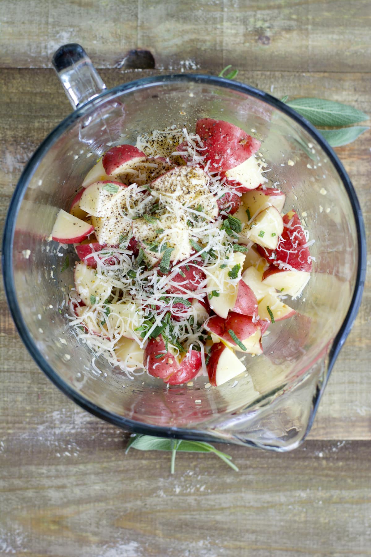 overhead view of chopped red potatoes in a glass mixing bowl with herbs and spices 