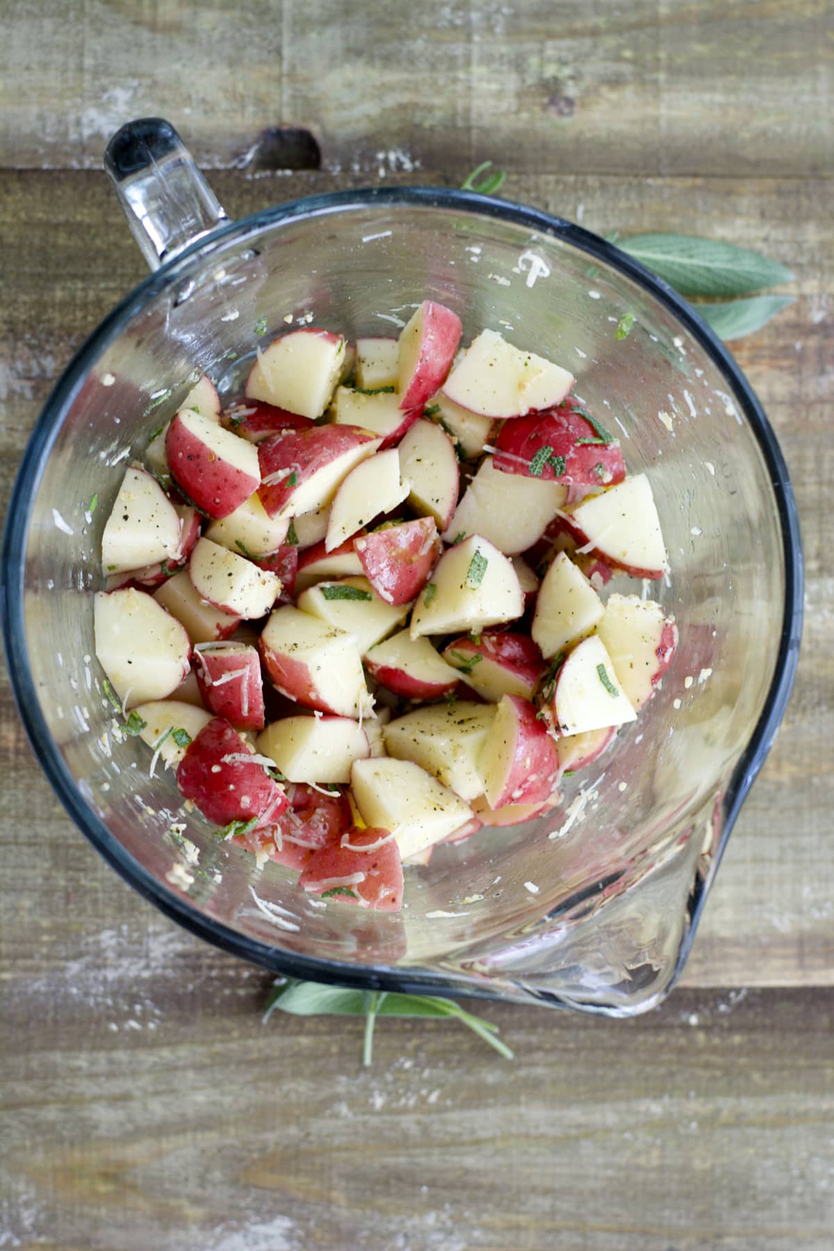 overhead view of chopped red potatoes in a glass mixing bowl with herbs and spices 