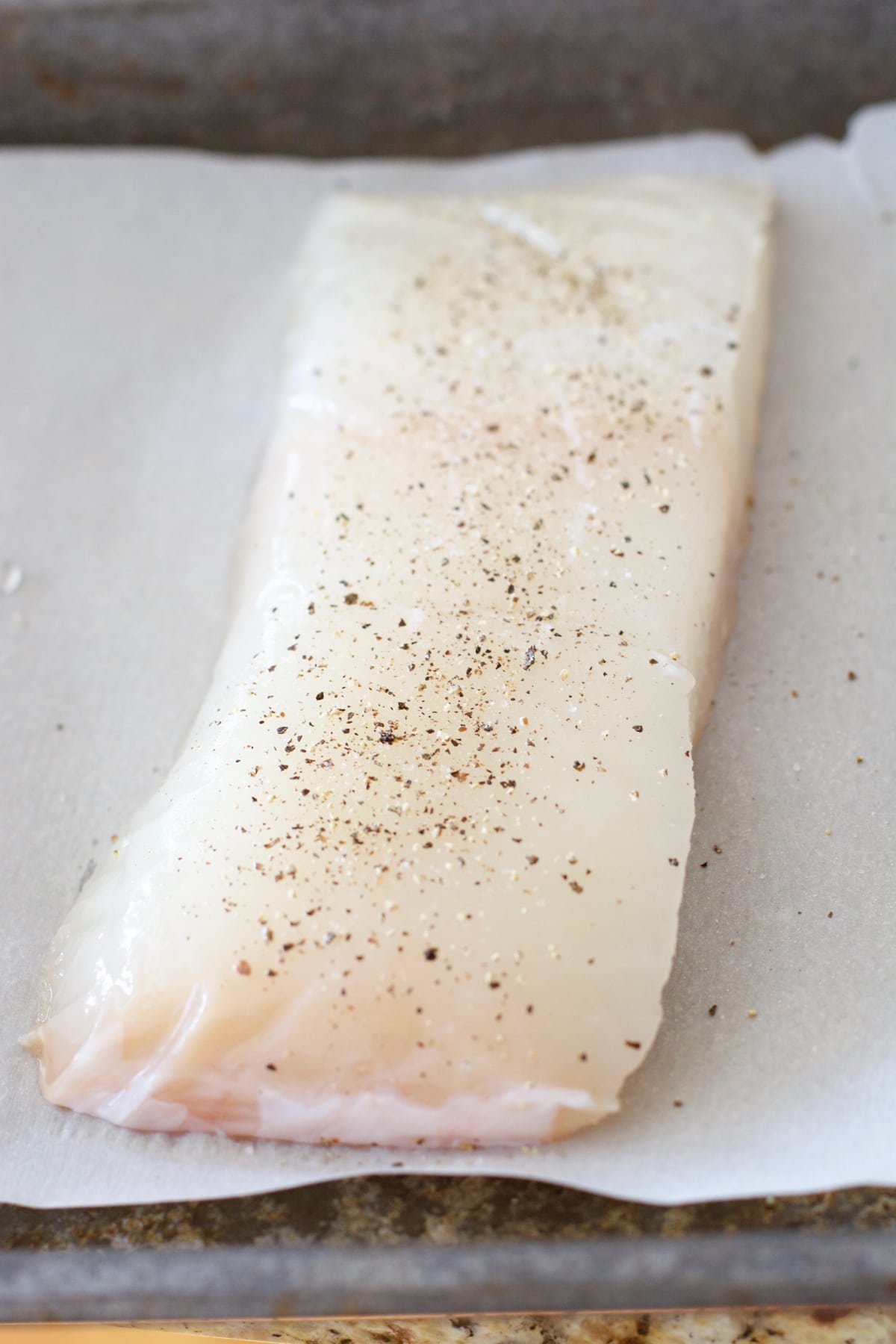 A raw halibut fillet on a piece of parchment paper. 