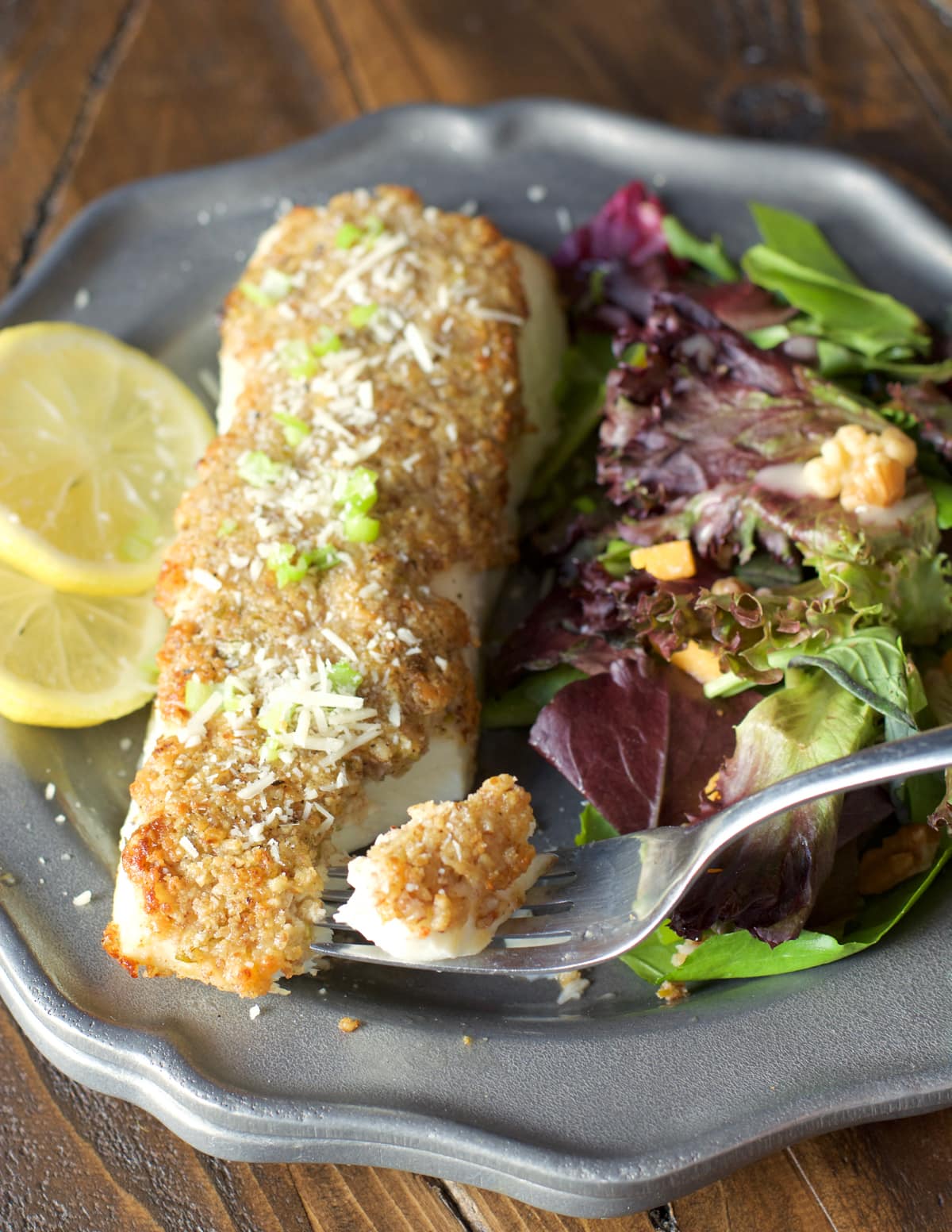 Pecan and Parmesan crusted halibut fillet on a dark plate with a side salad. 