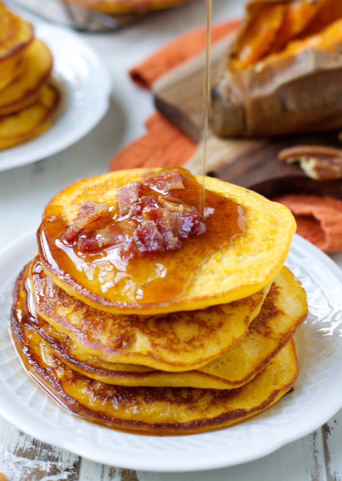 maple syrup being drizzled onto a stack of sweet potato bacon pancakes 