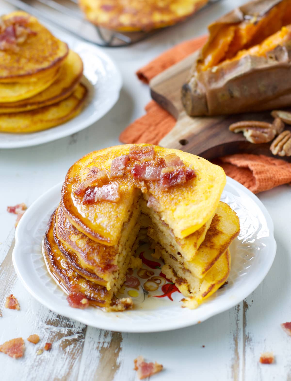 a stack of bacon sweet potato pancakes with a bite missing on a white plate 