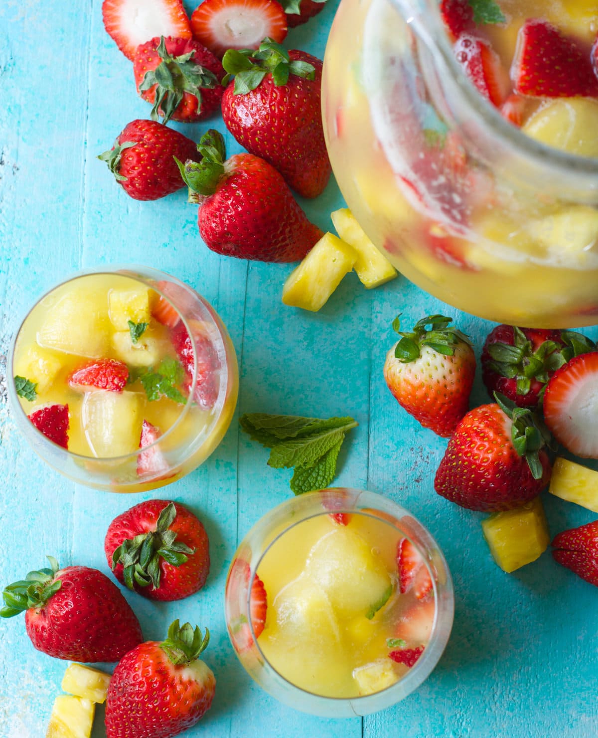 Overhead view of two glasses of non alcoholic punch, a pitcher of punch, and fresh fruit. 