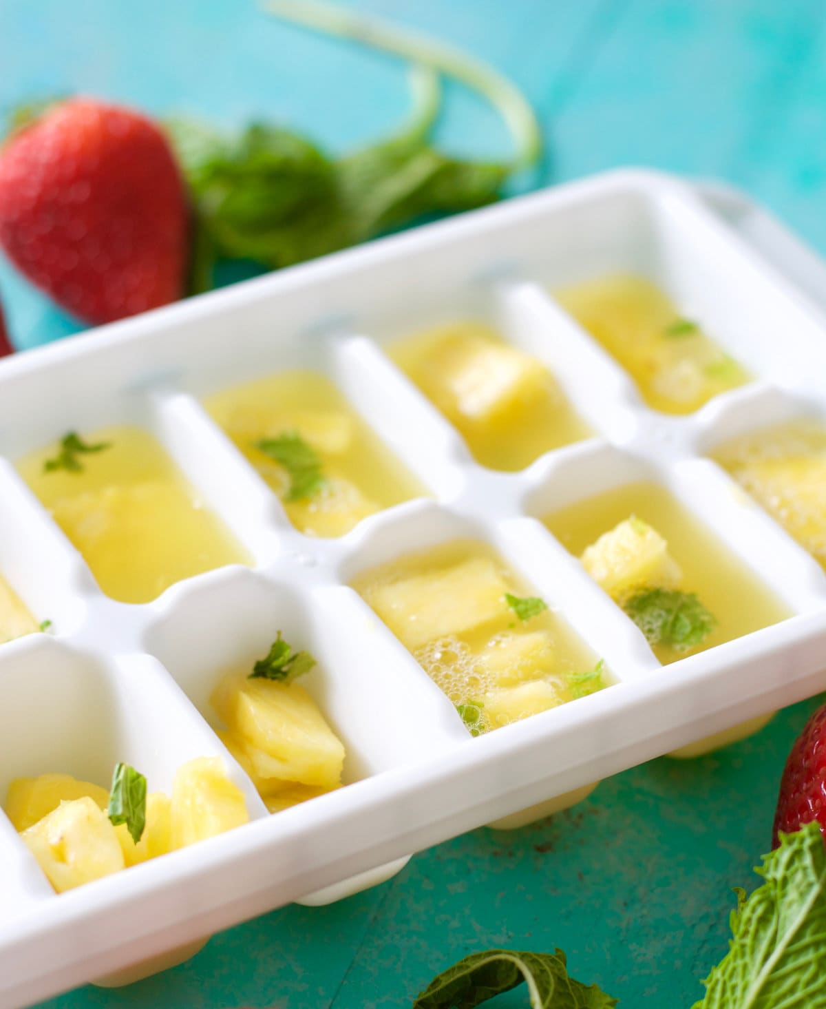 An ice cube tray filled with ginger ale, fresh pineapple chunks, and mint leaves. 