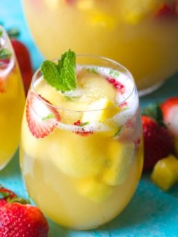 a tall glass of sparkling pineapple punch with fresh strawberries and mint
