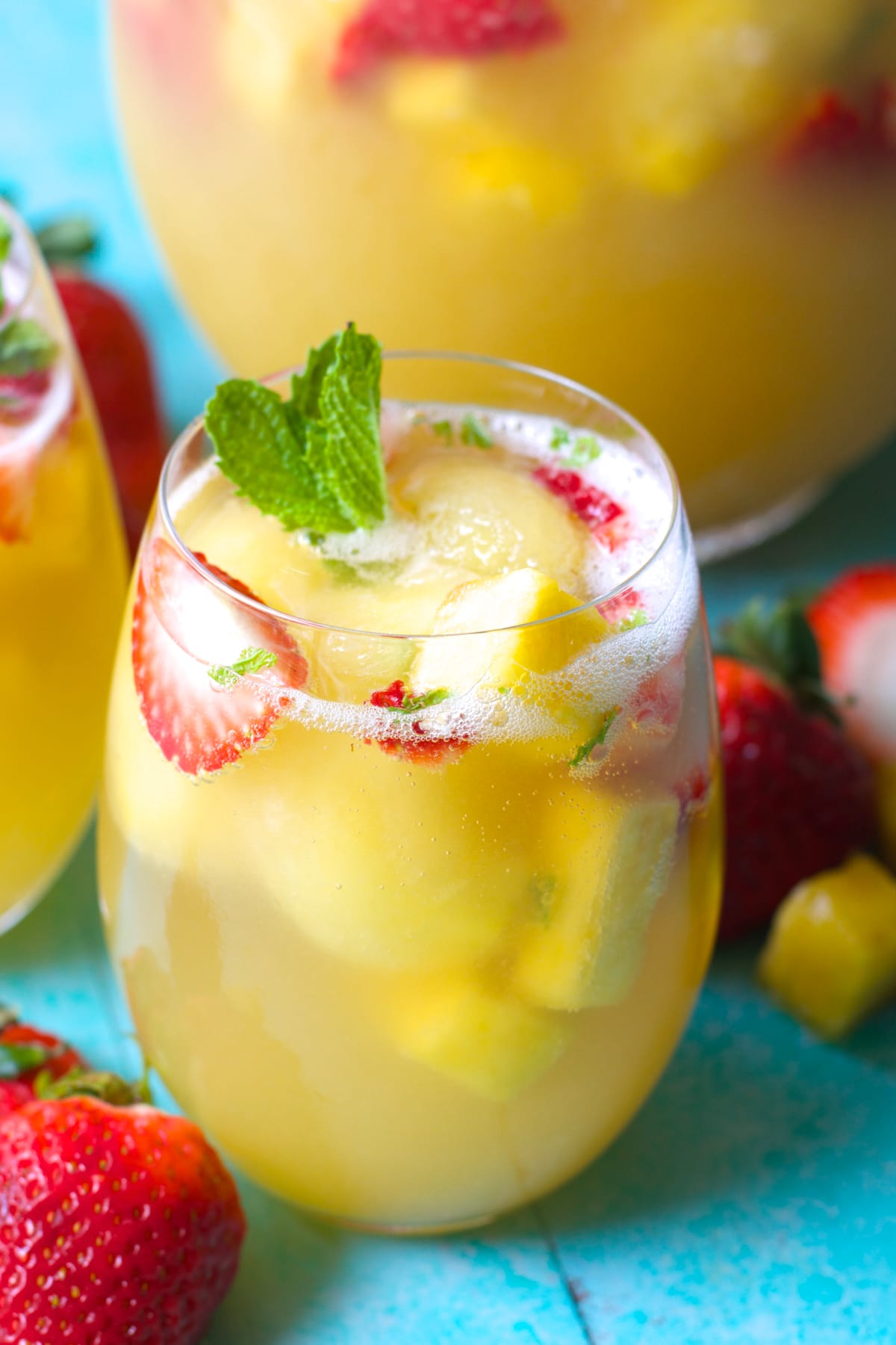 Close up of a glass of strawberry pineapple punch garnished with mint leaves and fresh fruit. 