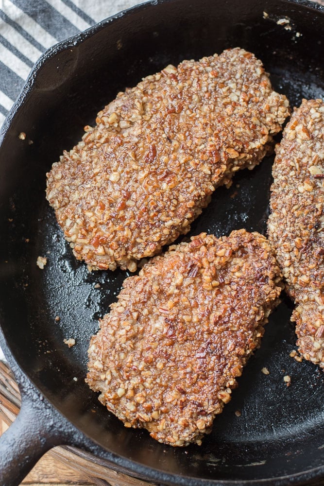 overhead view of three pecan crusted keto pork chops in a cast iron skillet 