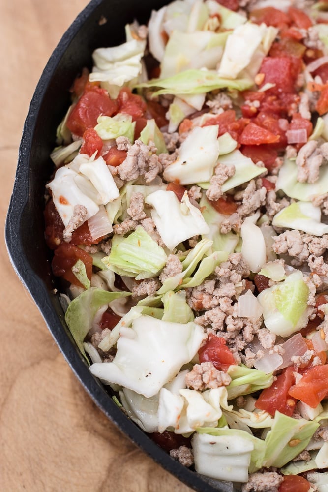 uncooked cabbage and tomatoes in a skillet with ground beef and onion 