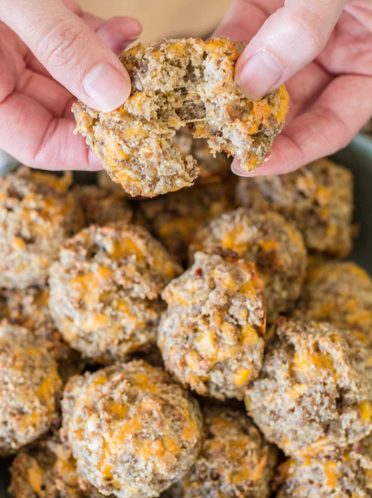 a gluten free sausage ball being torn in half above a bowl full of sausage balls 