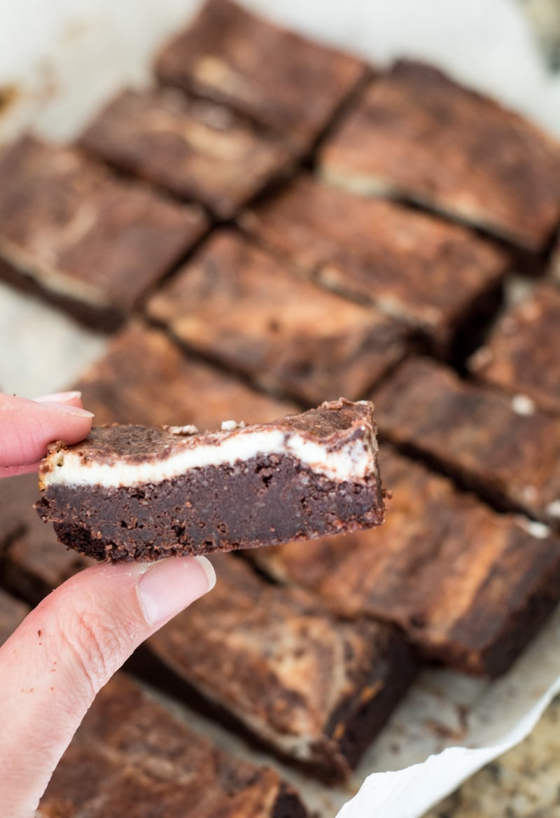 keto cheesecake brownie being held up above a pan of sliced brownies 