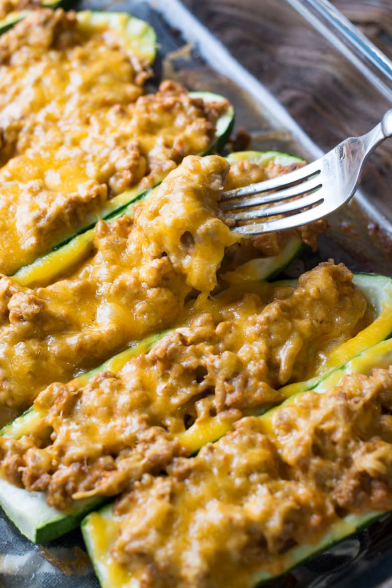 cheeseburger ground beef zucchini boats in a glass baking dish. A fork is being dug into one. 