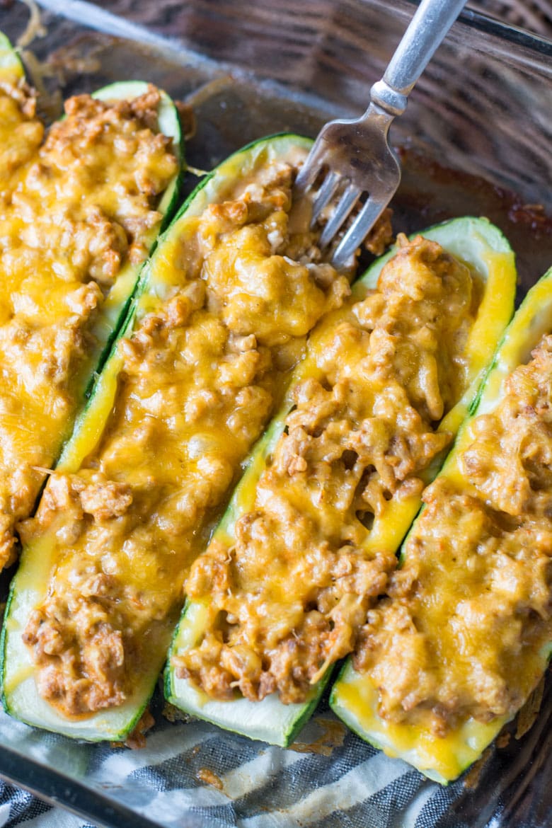 overhead view of keto zucchini boats in a baking dish. a fork is being dug into one. 