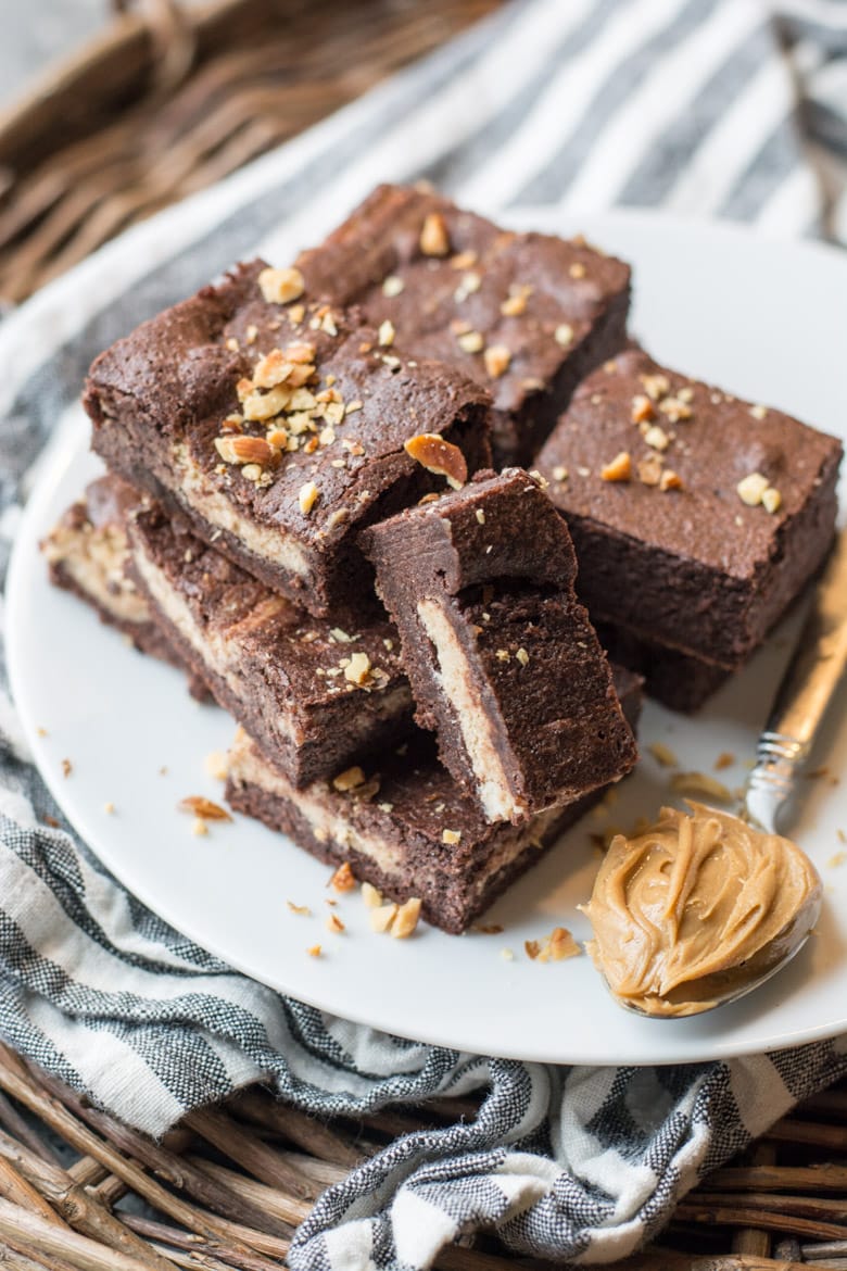 keto peanut butter brownies piled on a white plate next to a spoonful of peanut butter 