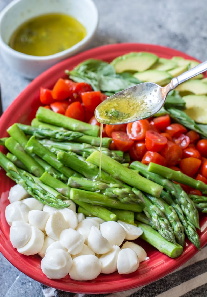 Lemon vinaigrette being drizzled over an asparagus, avocado, tomato salad