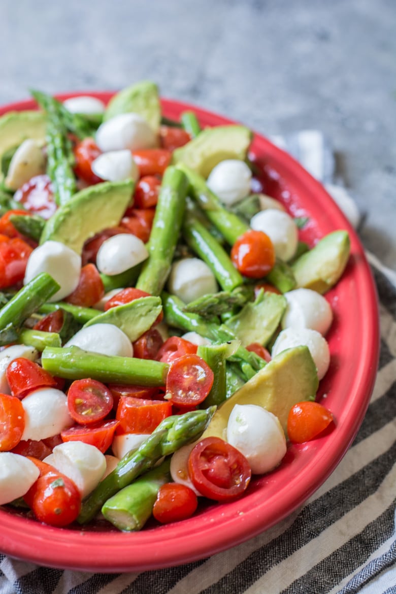 A cold asparagus salad made with tomatoes and mozzarella, in a red serving dish.