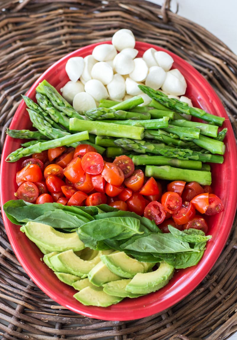 Overhead view of the ingredients for a cold asparagus salad in a red serving dish.