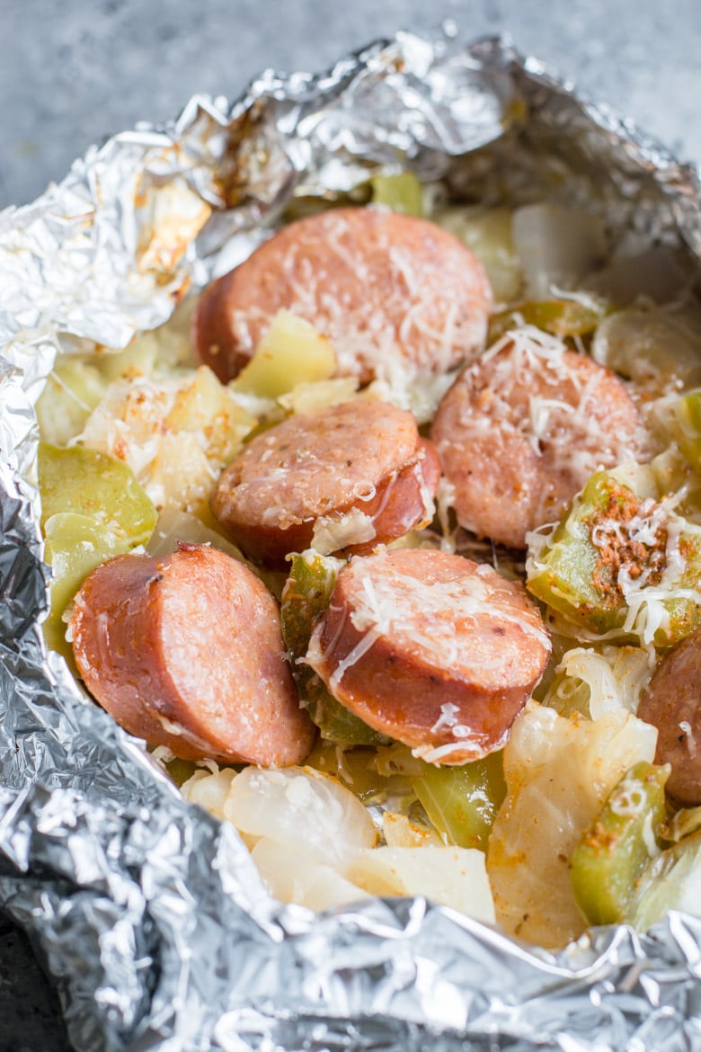 An open keto sausage and cabbage foil pack, sprinkled with Parmesan. 