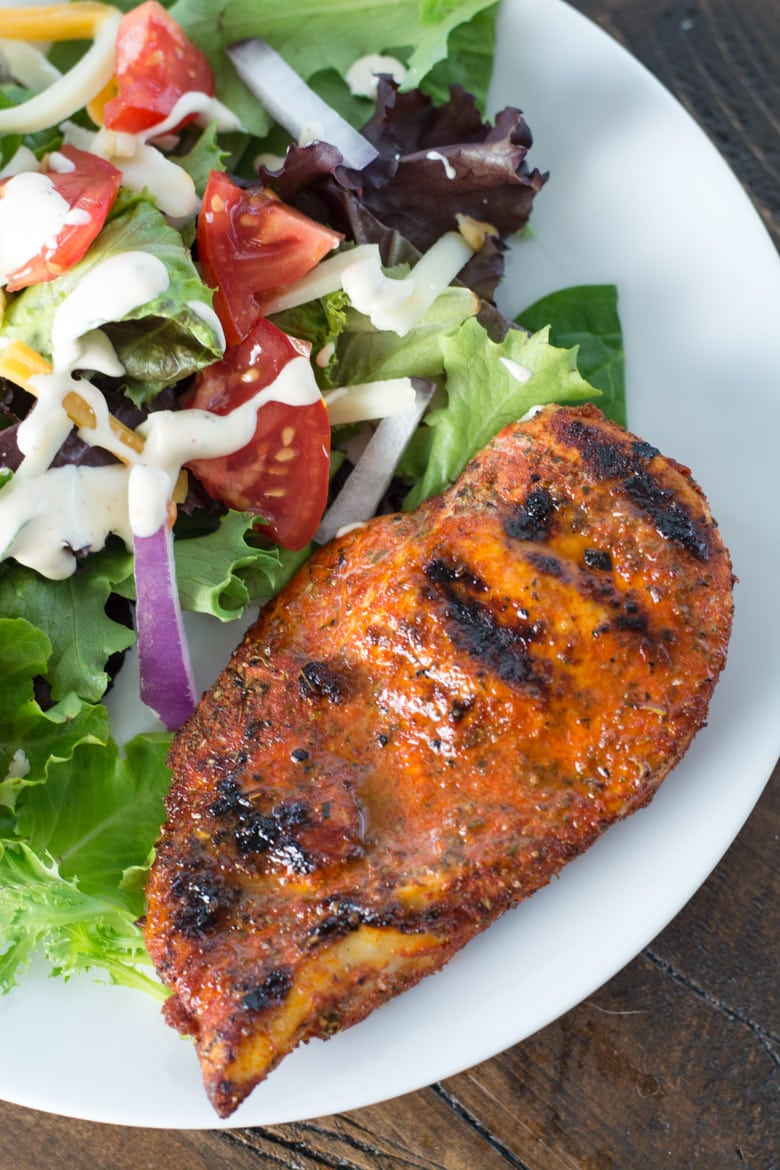 blackened chicken breast on white plate with a side salad