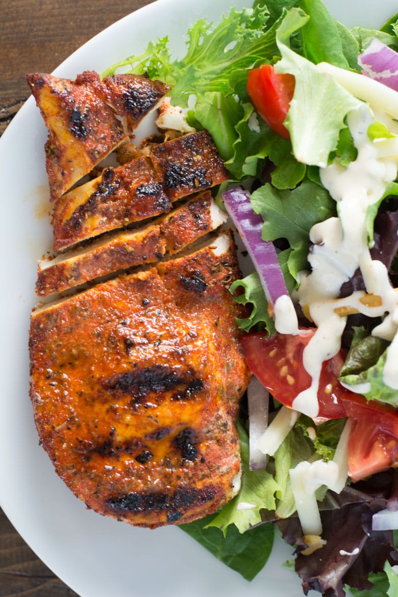 overhead view of partially sliced grilled blackened chicken breast on a white plate with a side salad