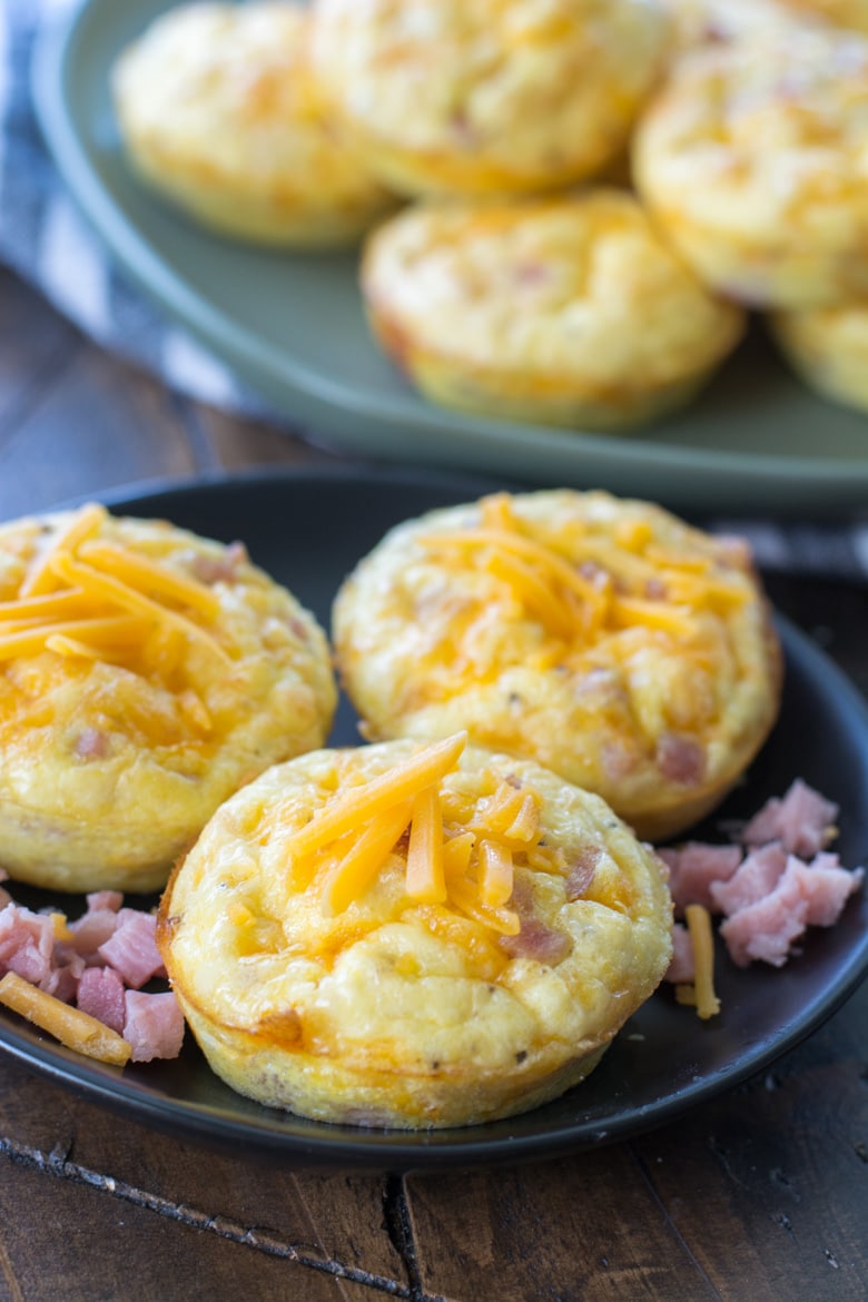 three ham and cheese keto egg muffins on a gray plate. More egg muffins rest in the background. 