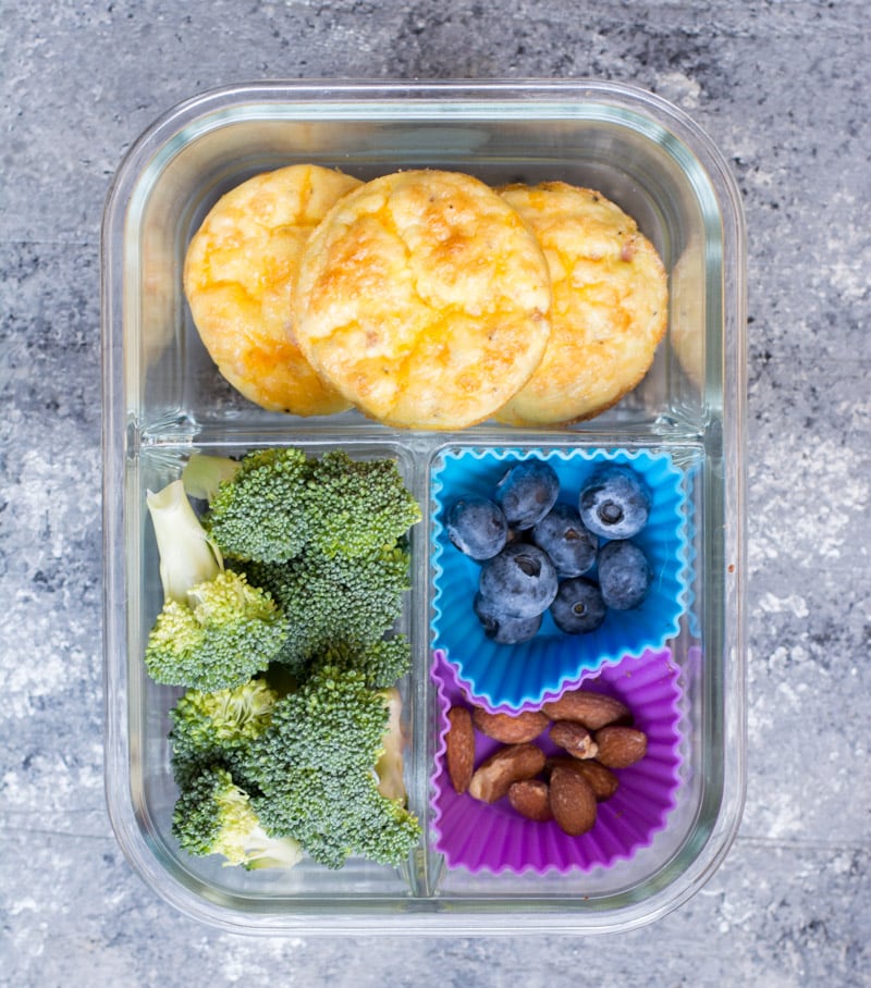 overhead view of a meal prep container with three low carb egg muffins, broccoli, berries, and nuts. 