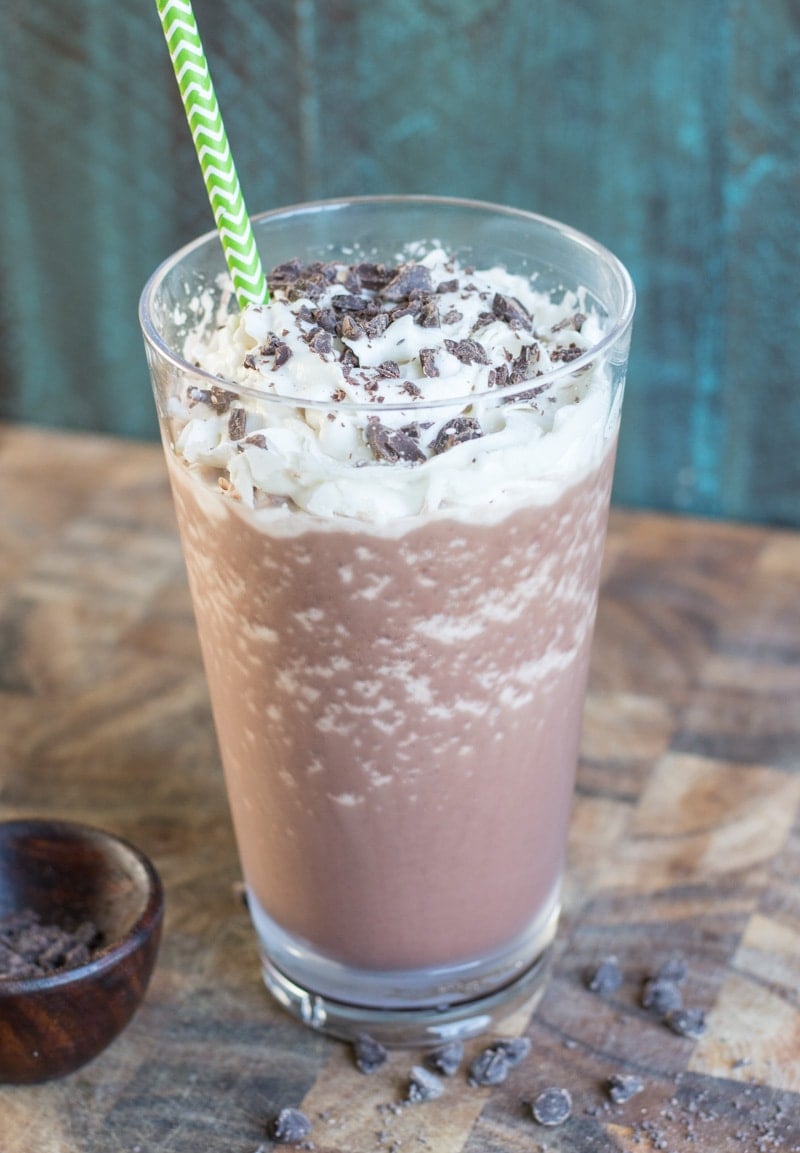 a glass of keto mocha frappuccino topped with whipped cream and chocolate shavings. A straw is poking out of the top. 