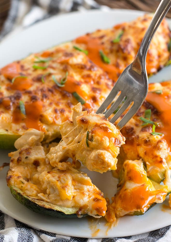 Two buffalo chicken zucchini boats on a white plate, being dug into with a fork. 