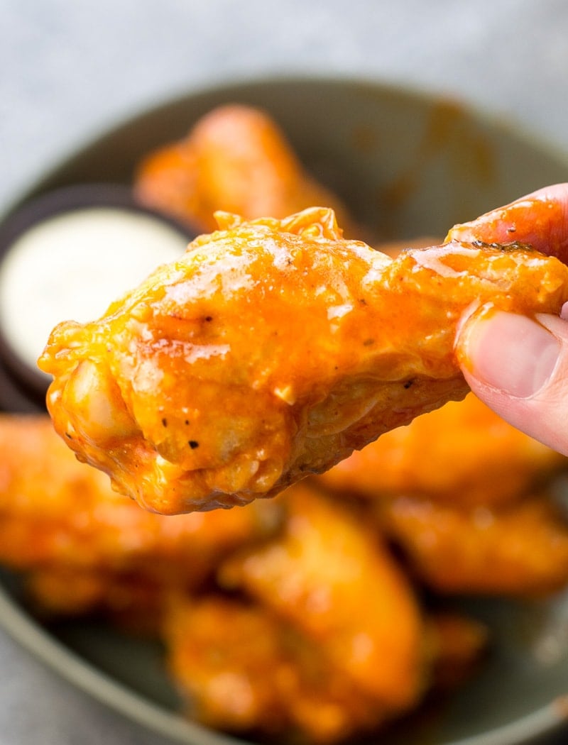 an air fryer buffalo wing being held aloft 