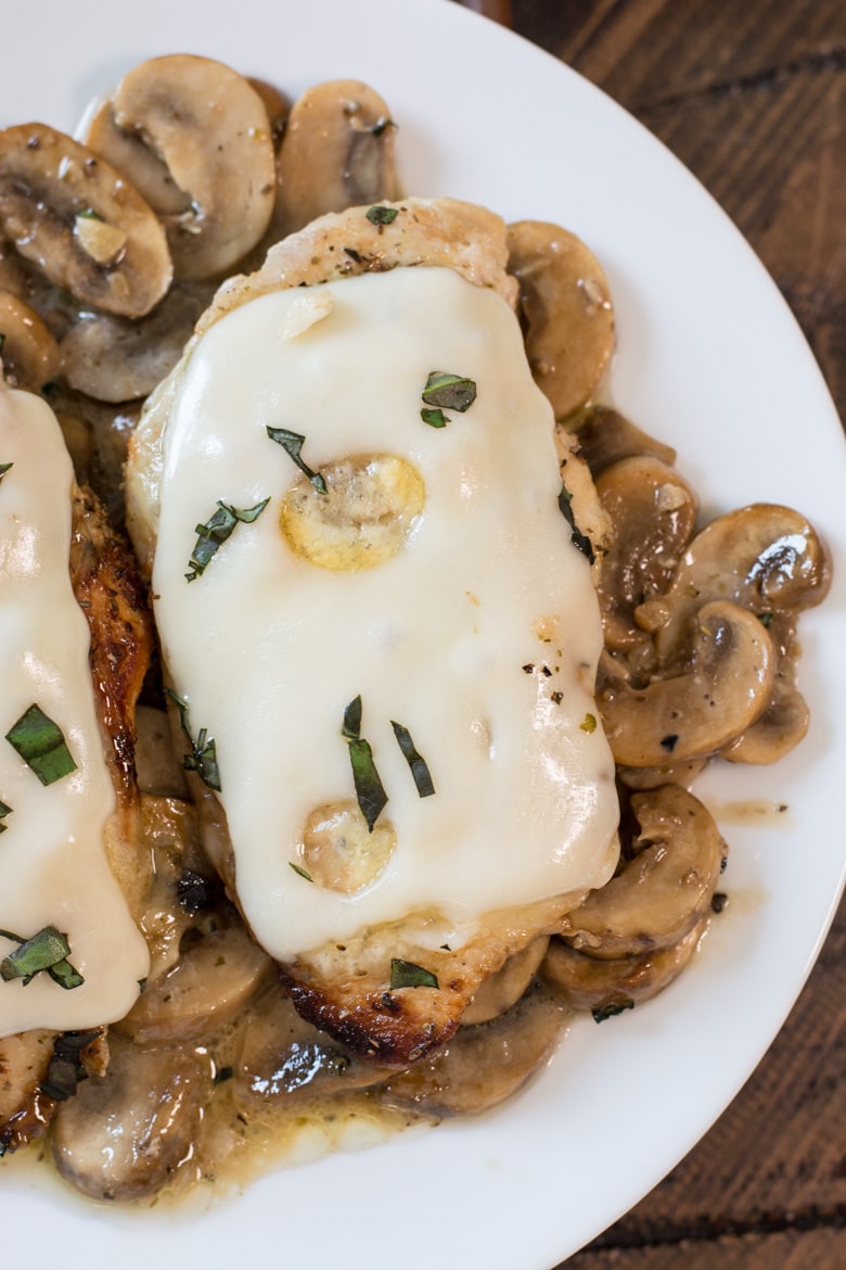 Chicken breast covered in melted swiss cheese and a creamy keto mushroom sauce on a white plate