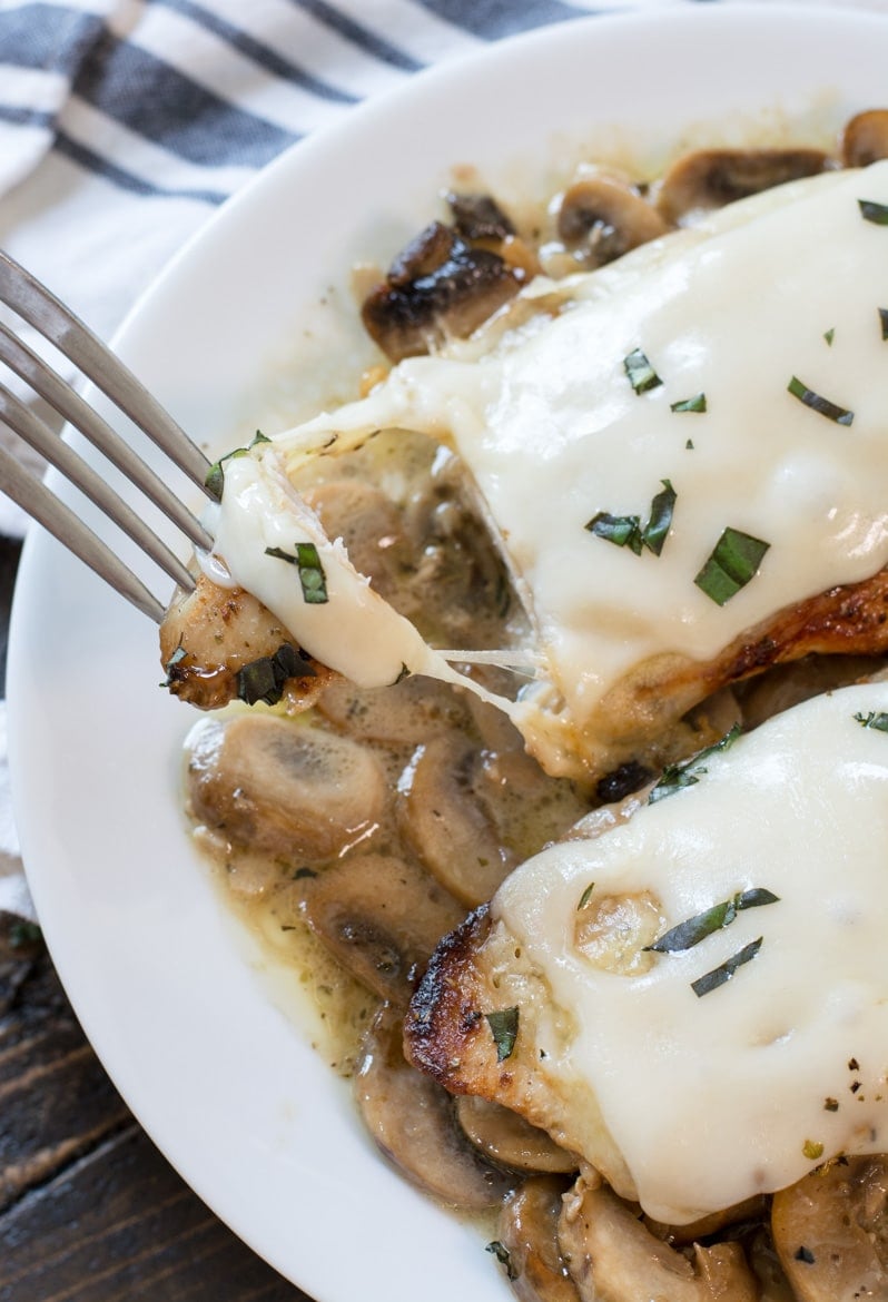 Two chicken breasts with mushroom sauce on a white plate. A piece is being removed by a fork. 