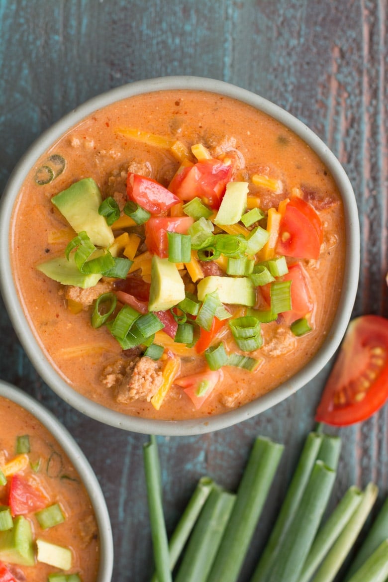 overhead shot of keto taco soup garnished with avocado, tomato, cheese, and green onions