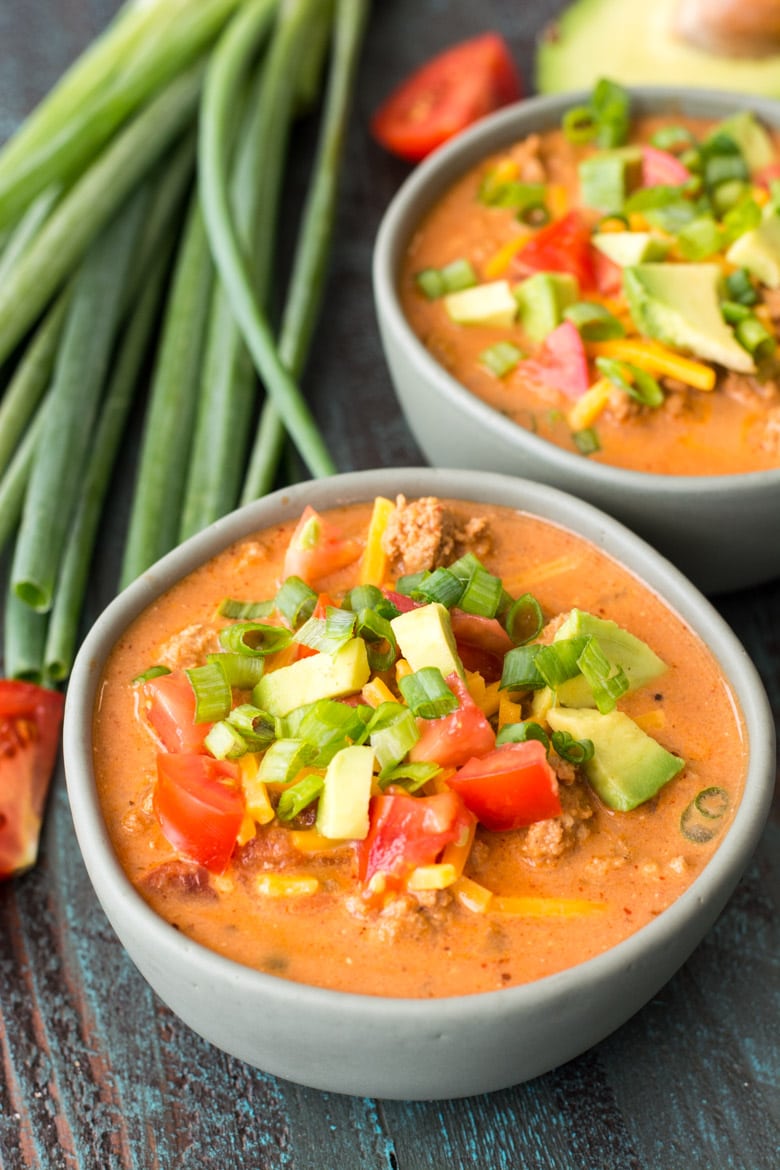 Two bowls of low carb taco soup next to a bunch of green onions. 