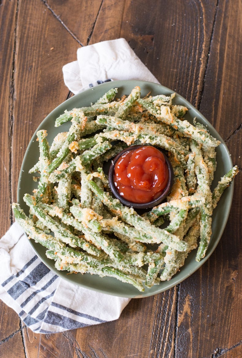 overhead view of a plate of green bean fries with a dish of ketchup in the center