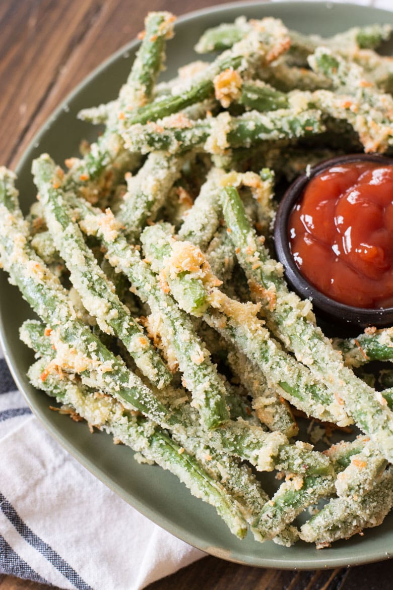 healthy green bean fries on a large plate with a dish of ketchup 