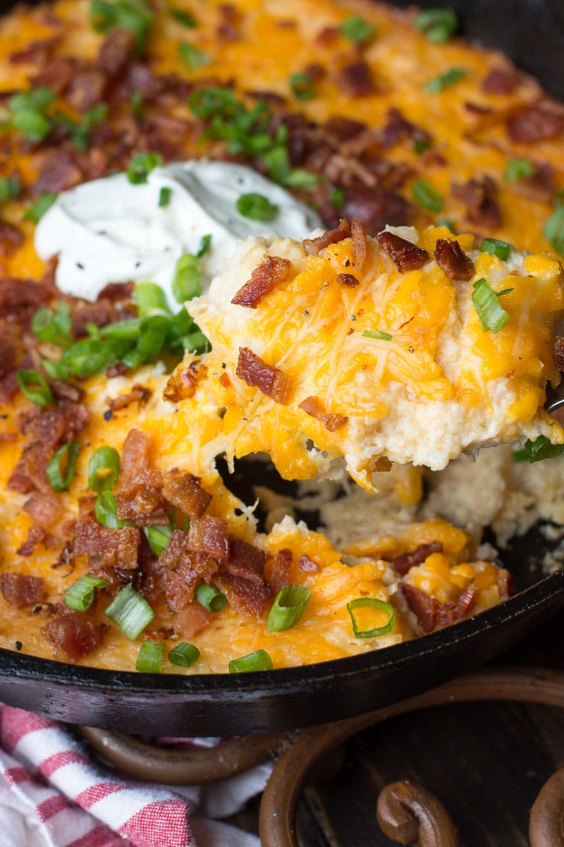 a portion of cauliflower bacon casserole being scooped from a skillet 