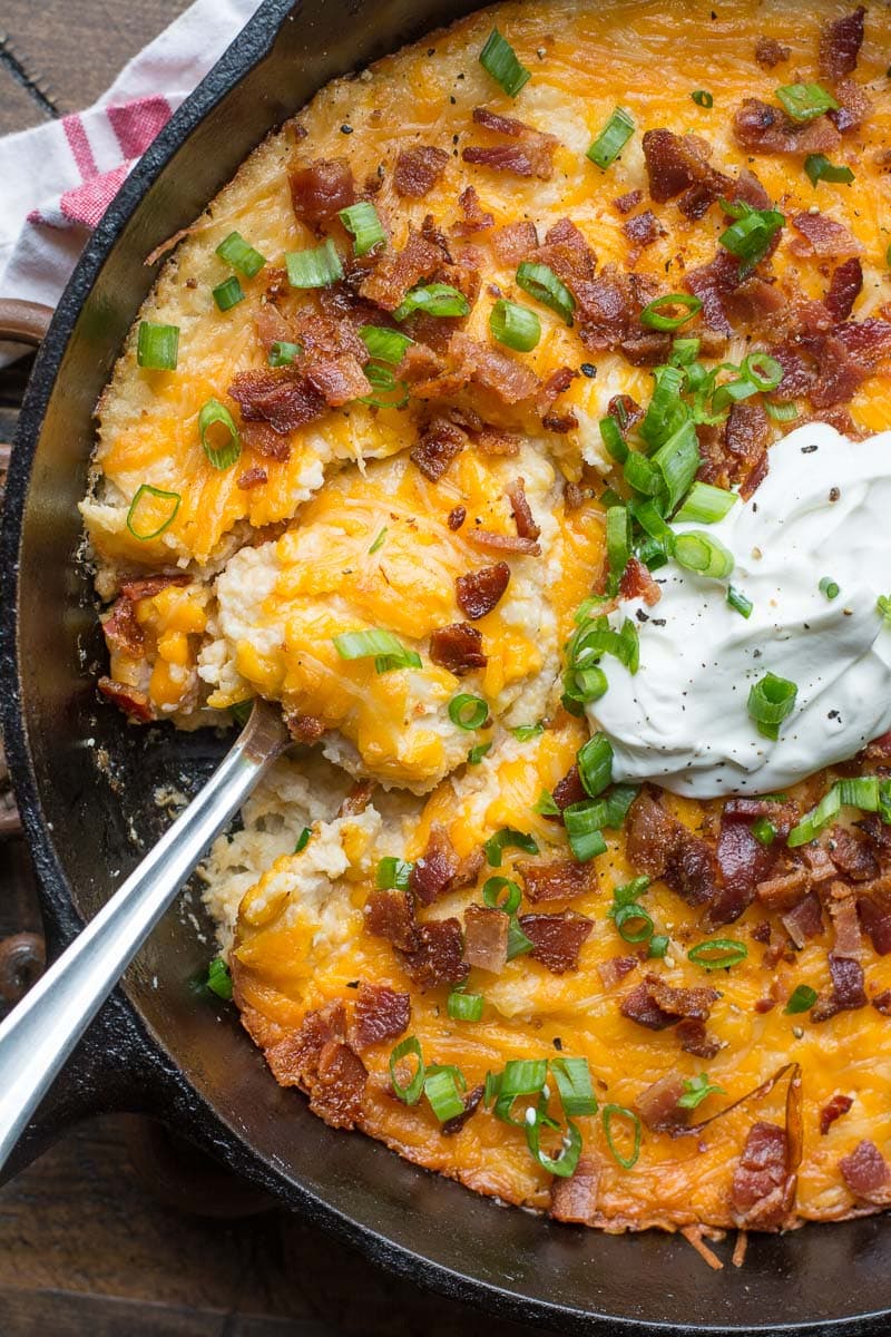 overhead view of cauliflower casserole topped with bacon, green onions, and sour cream 